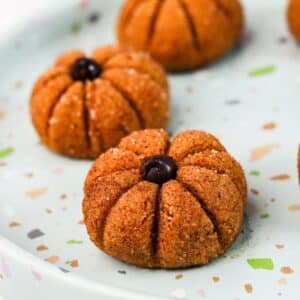 Pumpkin-shaped energy bites with ridged sides and a chocolate chip stem, arranged on a speckled plate.