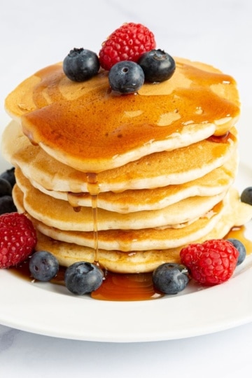 Stack of pancakes with syrup and berries. Featured image for 11 High Protein Calorie Deficit Breakfast Ideas blog post on OliviaWyles.com
