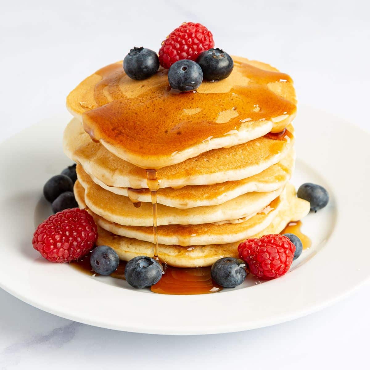 Stack of pancakes with syrup and berries. Featured image for 11 High Protein Calorie Deficit Breakfast Ideas blog post on OliviaWyles.com