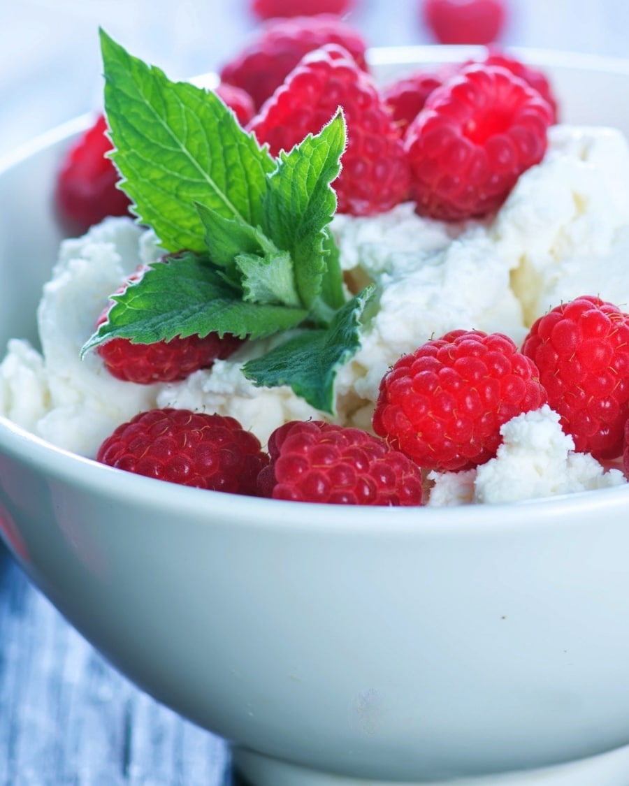 Bowl of cottage cheese topped with fresh raspberries and mint leaves. High protein, low calorie breakfast idea for weight loss and calorie deficit meal planning.