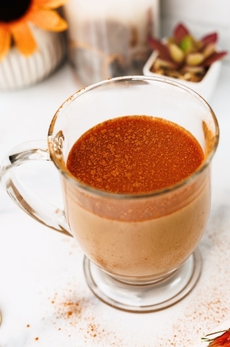 Glass mug of chai latte topped with a dusting of cinnamon on a white background.