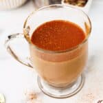Close-up of chai latte in a clear mug with a cinnamon topping and scattered cinnamon on the table.