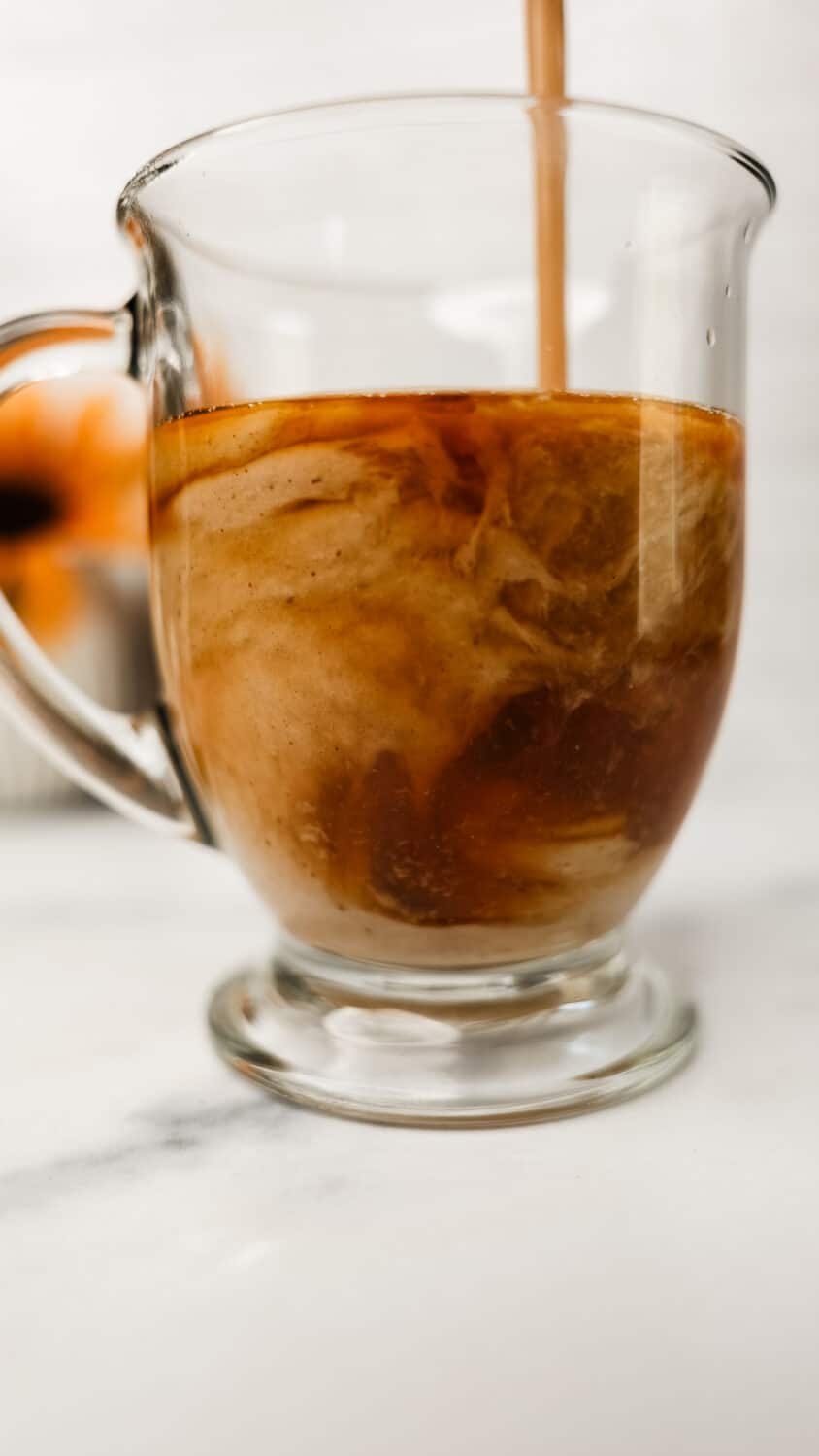 Protein chai latte being poured into a clear mug, swirling with tea.