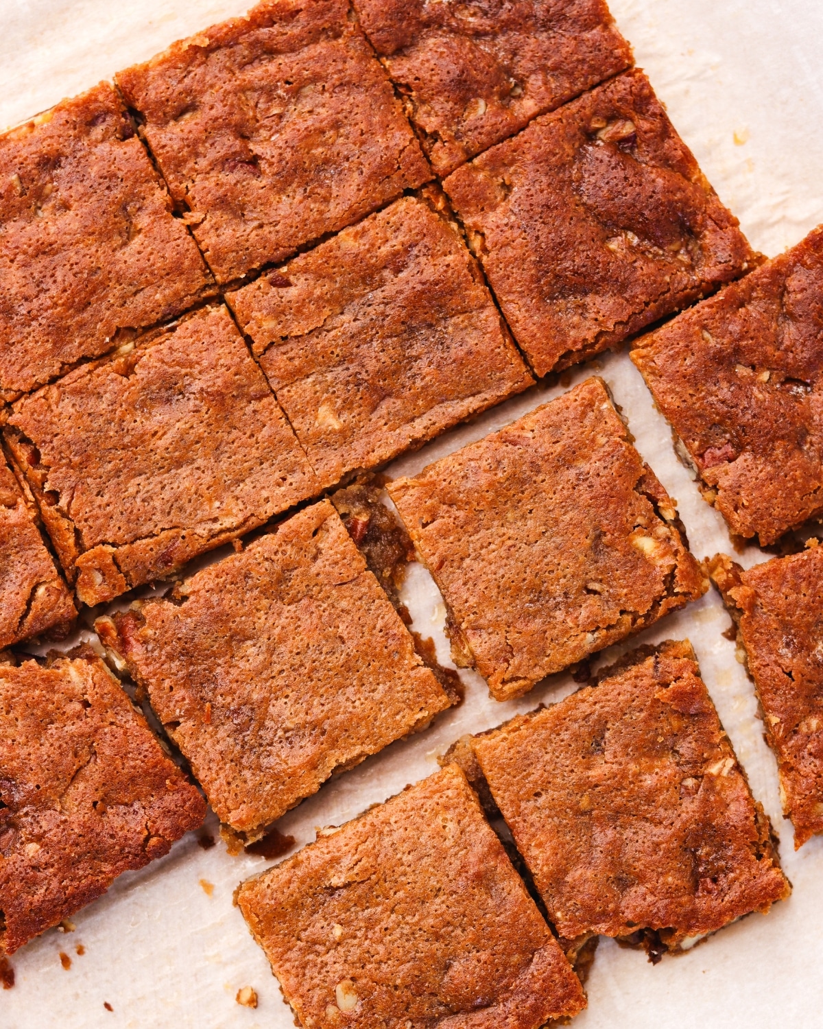 Baked protein maple pecan blondies cut into squares on parchment paper.