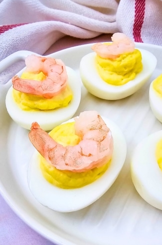Close-up of shrimp deviled eggs on a white plate with a red-striped towel in the background.