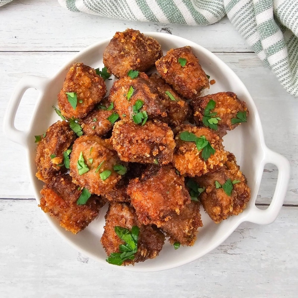 Plate of golden brown fried steak nuggets garnished with chopped parsley.