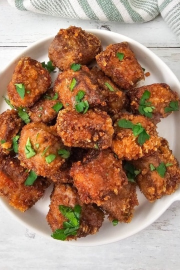 Plate of golden brown fried steak nuggets garnished with chopped parsley.