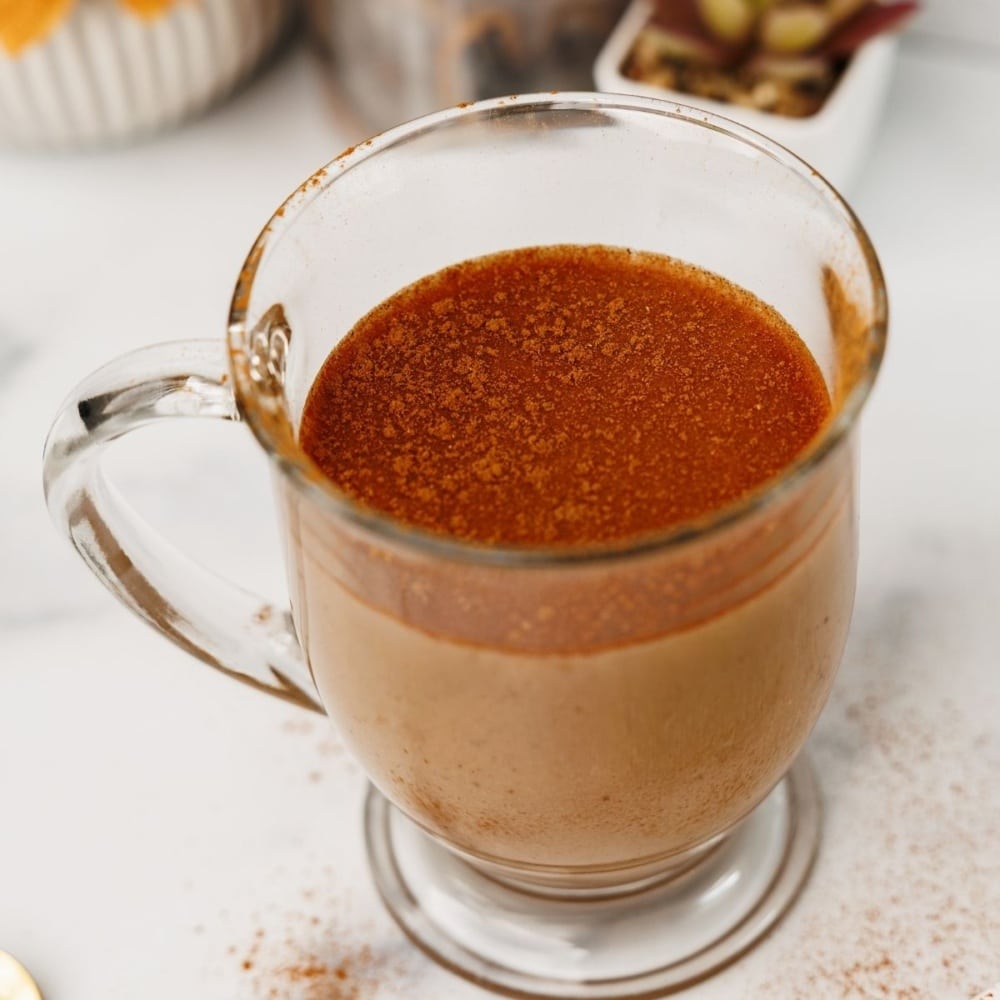 Glass mug of chai latte topped with a dusting of cinnamon on a white background.