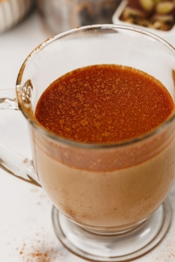 Glass mug of chai latte topped with a dusting of cinnamon on a white background.
