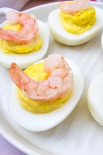 Close-up of shrimp deviled eggs on a white plate with a red-striped towel in the background.