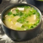 Two bowls of miso soup with tofu and scallions on a linen cloth
