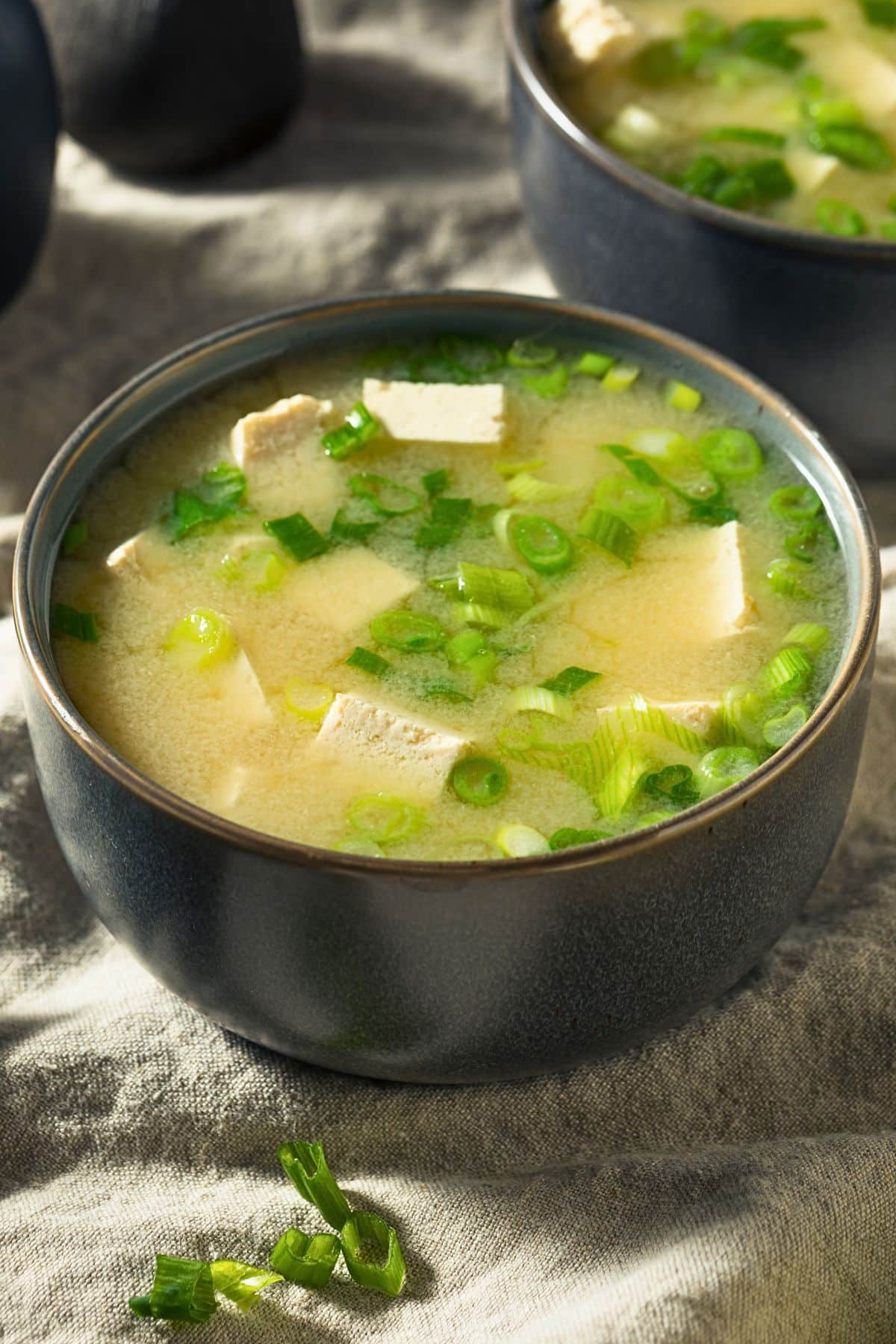Two bowls of miso soup with tofu and scallions on a linen cloth