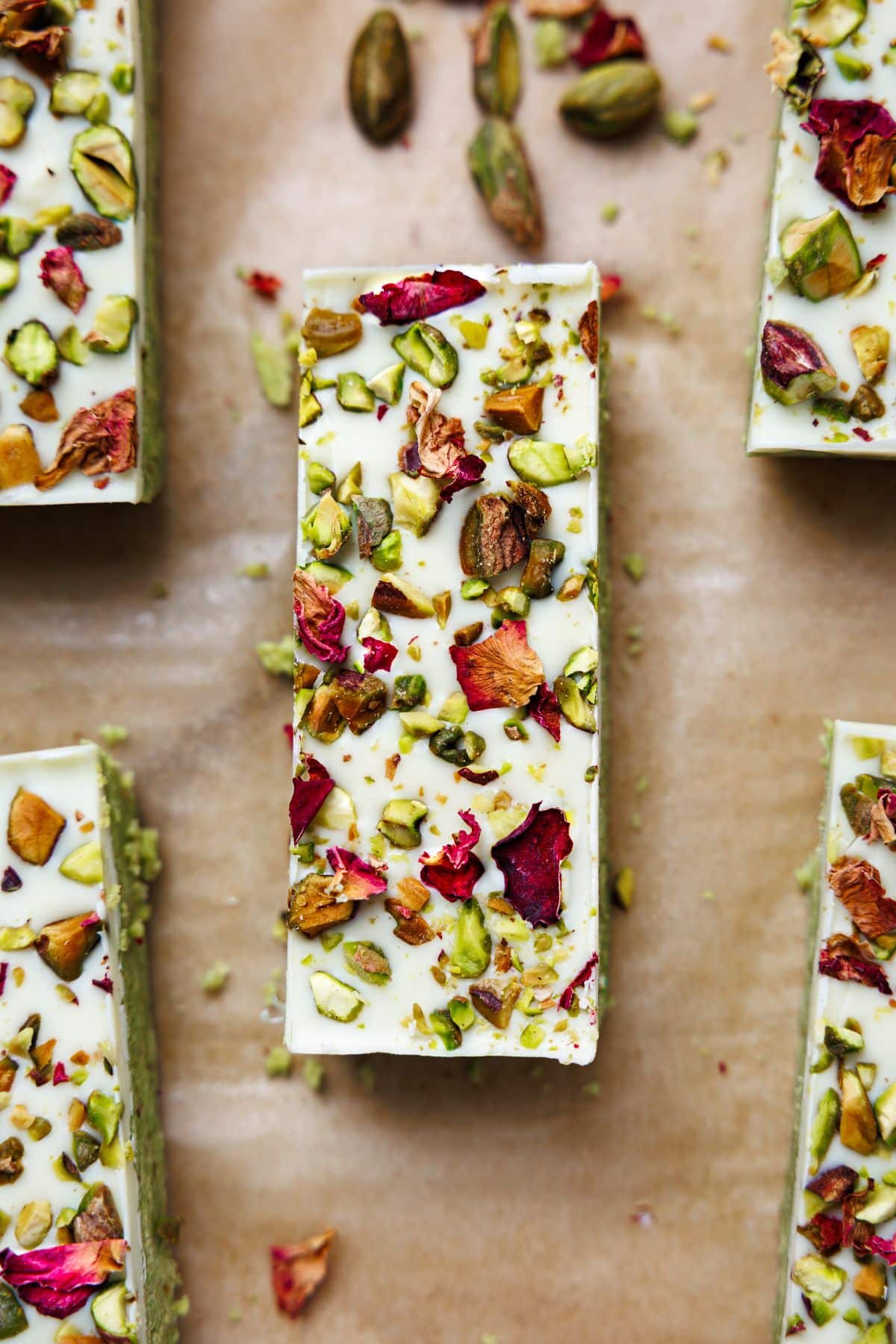 White chocolate covered pistachio protein bars topped with chopped pistachios and dried rose petals on parchment paper
