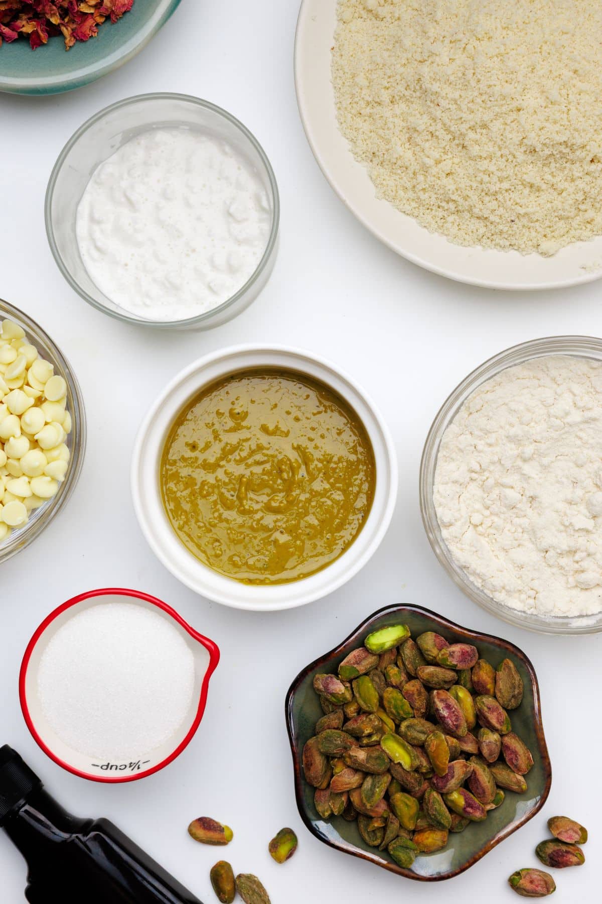 Overhead view of ingredients for pistachio protein bars including almond flour, protein powder, nut butter, white chocolate chips, pistachios, and Greek yogurt in separate bowls