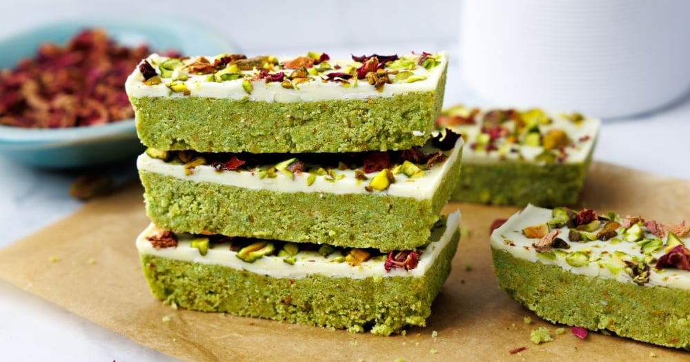 Stack of three pistachio protein bars showing bright green base layer with white chocolate topping decorated with pistachios and rose petals
