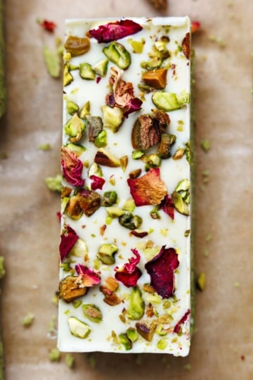 Close-up overhead view of single pistachio protein bar showing white chocolate coating with chopped pistachios and dried rose petal garnish
