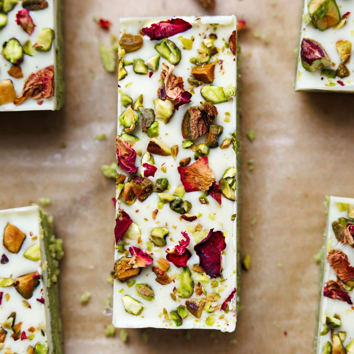 Close-up overhead view of single pistachio protein bar showing white chocolate coating with chopped pistachios and dried rose petal garnish