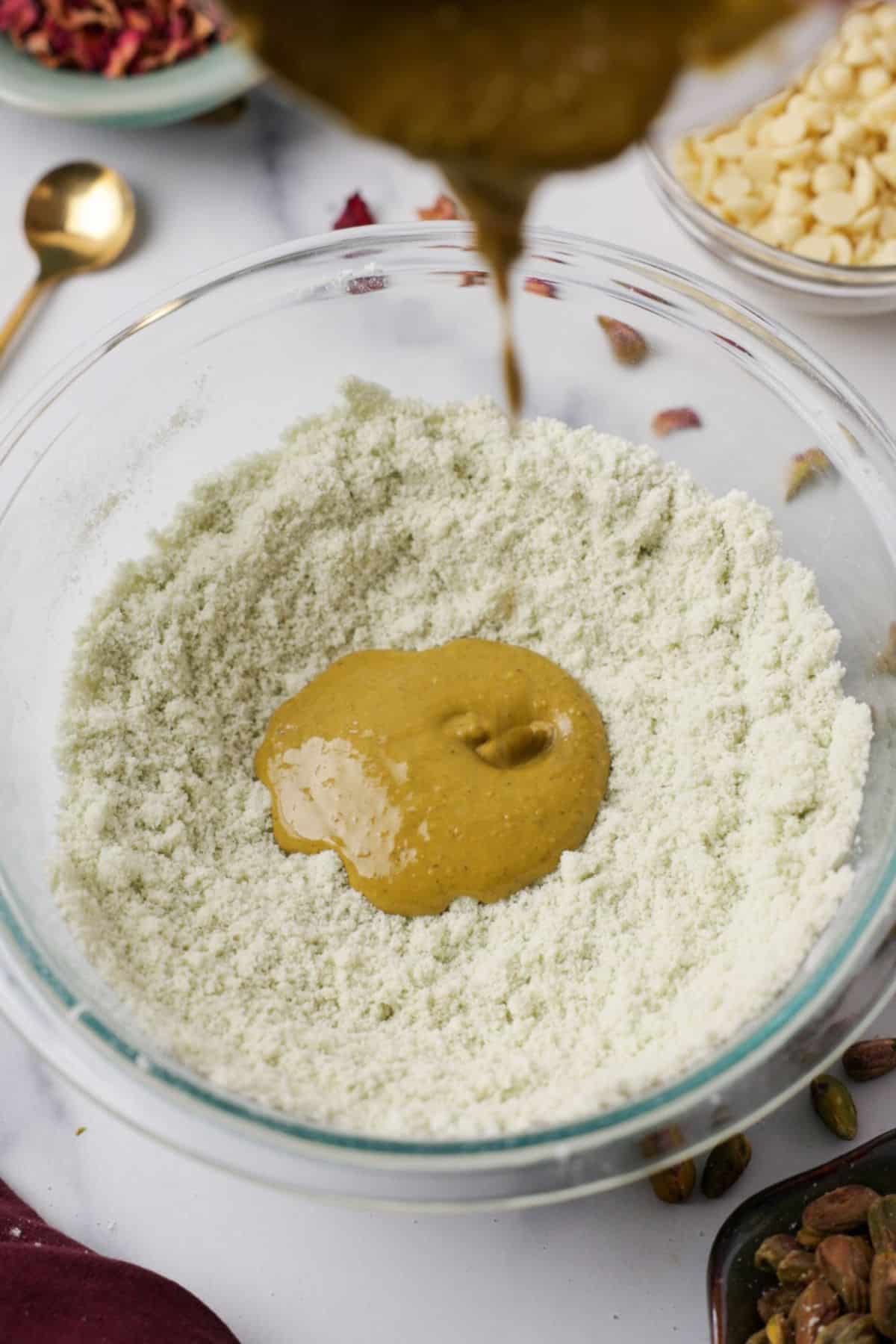 Nut butter being drizzled into bowl of almond flour and pistachio powder mixture