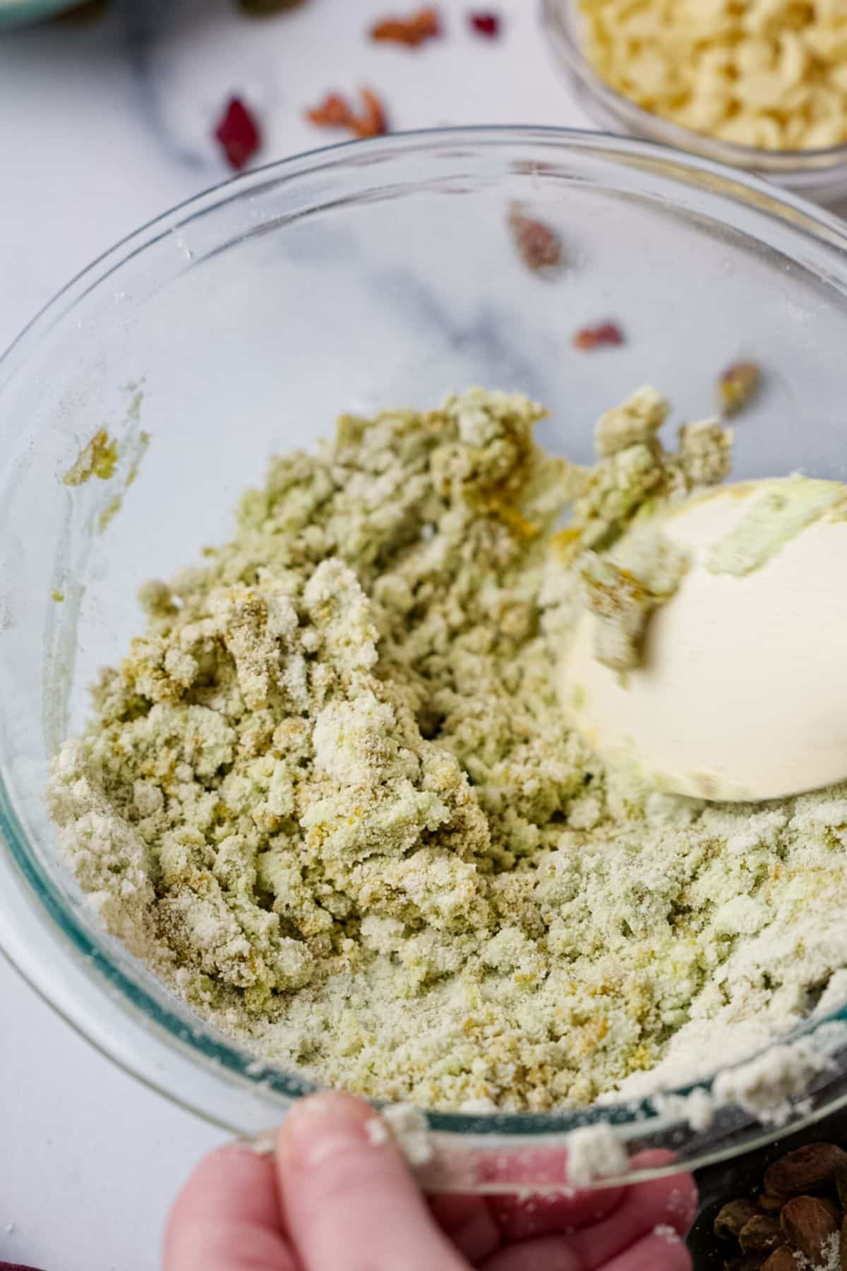 Green pistachio protein bar dough being mixed with white spatula in glass bowl