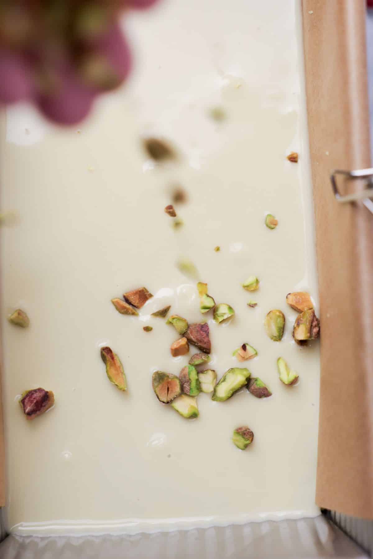 Chopped pistachios and dried rose petals being sprinkled onto white chocolate layer