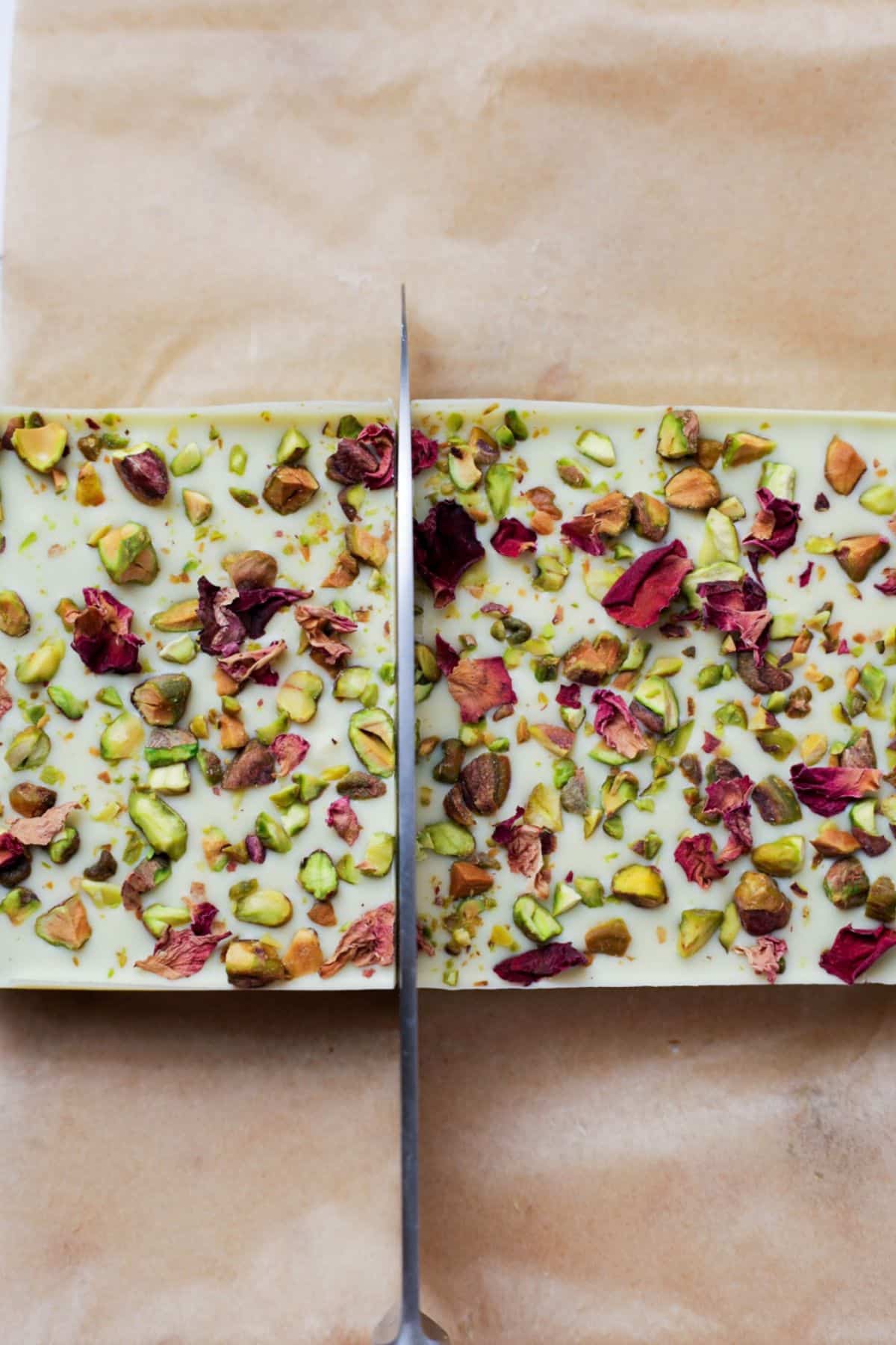 Large knife cutting through white chocolate topped pistachio bars in loaf pan