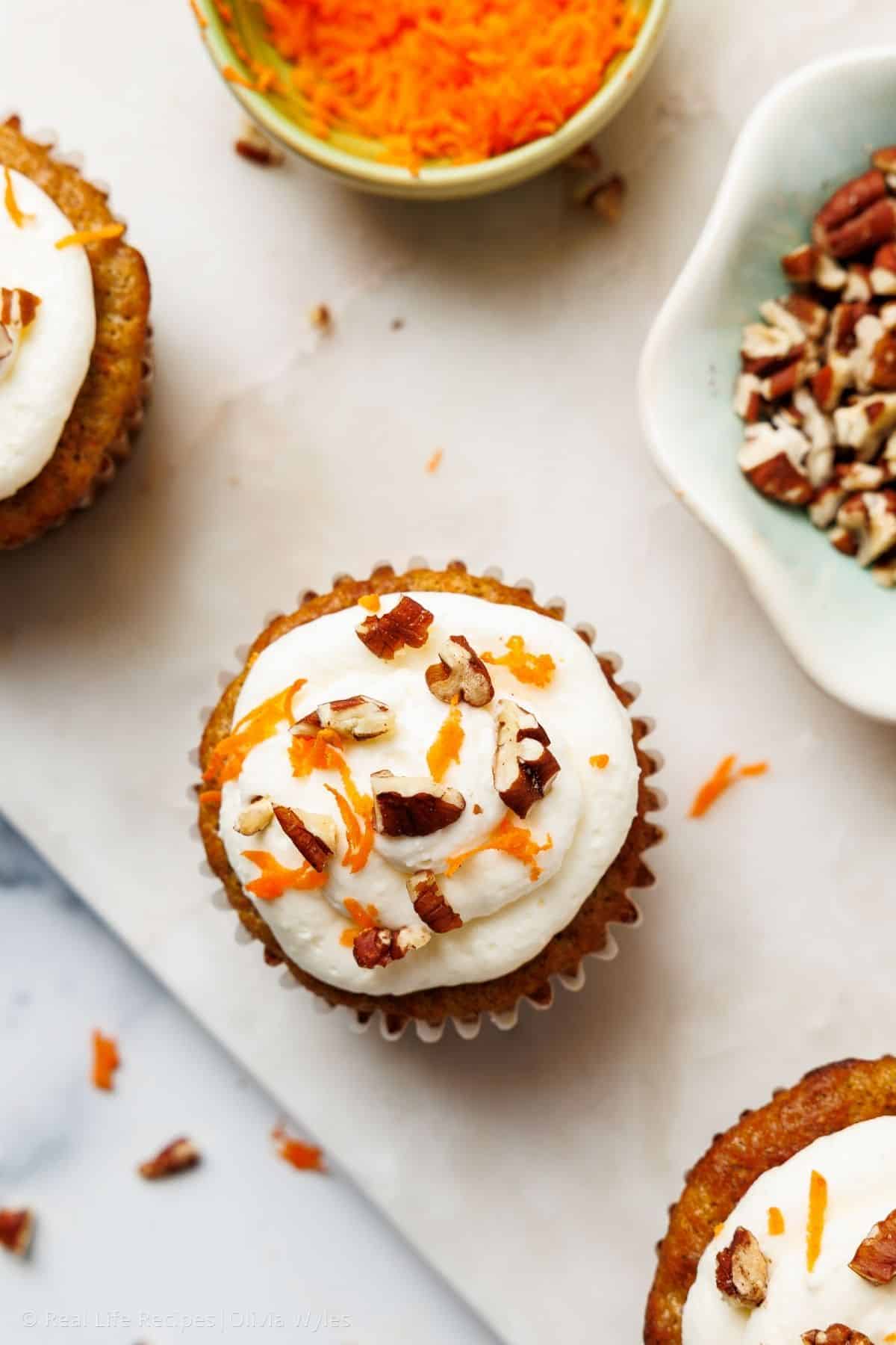 Overhead view of a frosted carrot cake cupcake with cream cheese frosting and chopped pecans on marble
