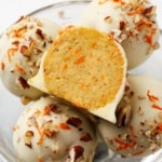 Keto carrot cake bites coated in white chocolate with chopped pecans and shredded carrot, one bitten to reveal the inside