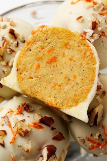 Keto carrot cake bites coated in white chocolate with chopped pecans and shredded carrot, one bitten to reveal the inside
