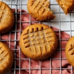 Single keto peanut butter cookie in focus on a wire rack over a rust napkin, with a deep criss-cross fork pattern.