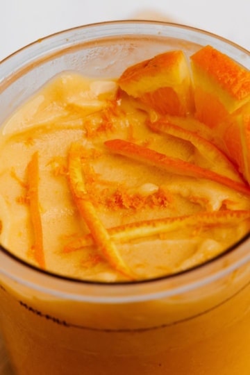 Orange creamsicle protein ice cream in Ninja Creami container topped with fresh orange slices