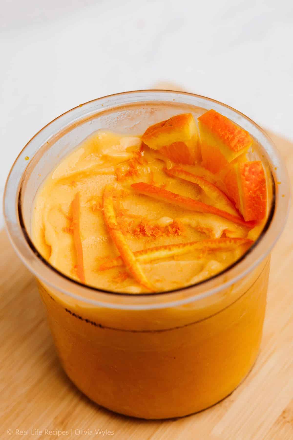 Creamy orange protein ice cream in Ninja Creami pint with orange slices on top viewed from above