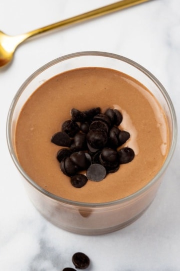 Creamy cottage cheese chocolate pudding topped with dark chocolate chips in a small jar on marble.