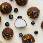 Overhead view of chocolate-coated blueberry lemon truffles on a marble surface, one cut in half to reveal a creamy white filling, scattered with fresh blueberries and lemon zest