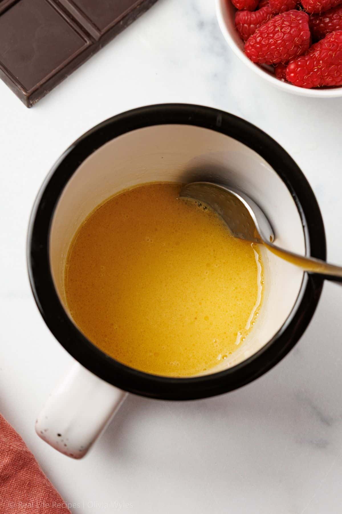 Overhead view of melted butter and beaten egg in a black and white ceramic mug, the first step in making a keto chocolate mug cake