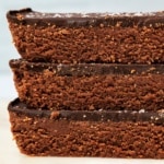 Three chocolate protein bars stacked sideways, showing layers of fudgy texture and chocolate topping.