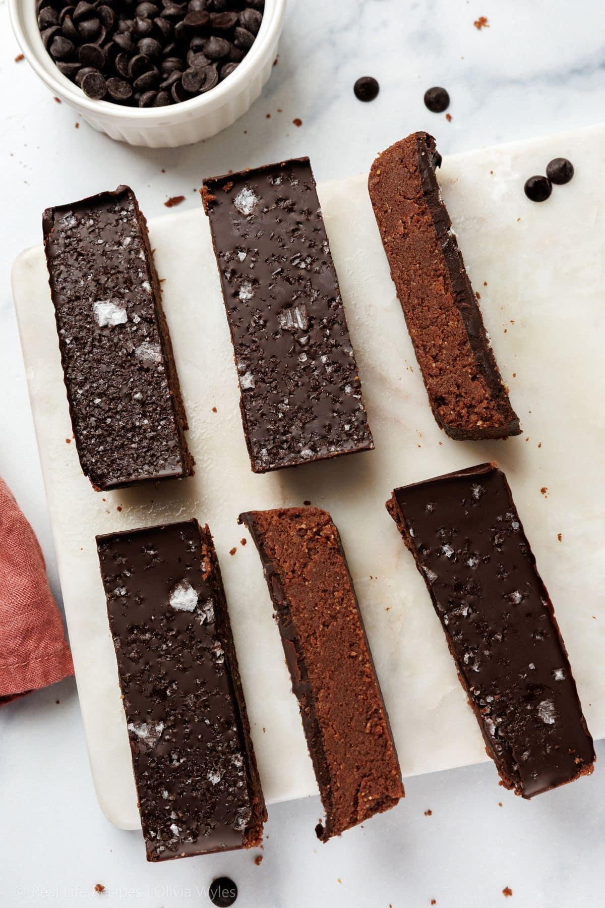 Overhead view of sliced chocolate protein bars on a marble board with chocolate chips scattered around.