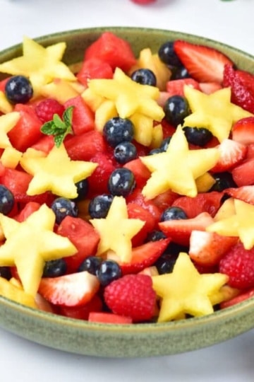 Patriotic fruit salad with strawberries, blueberries, raspberries, and star-shaped pineapple in a green bowl.