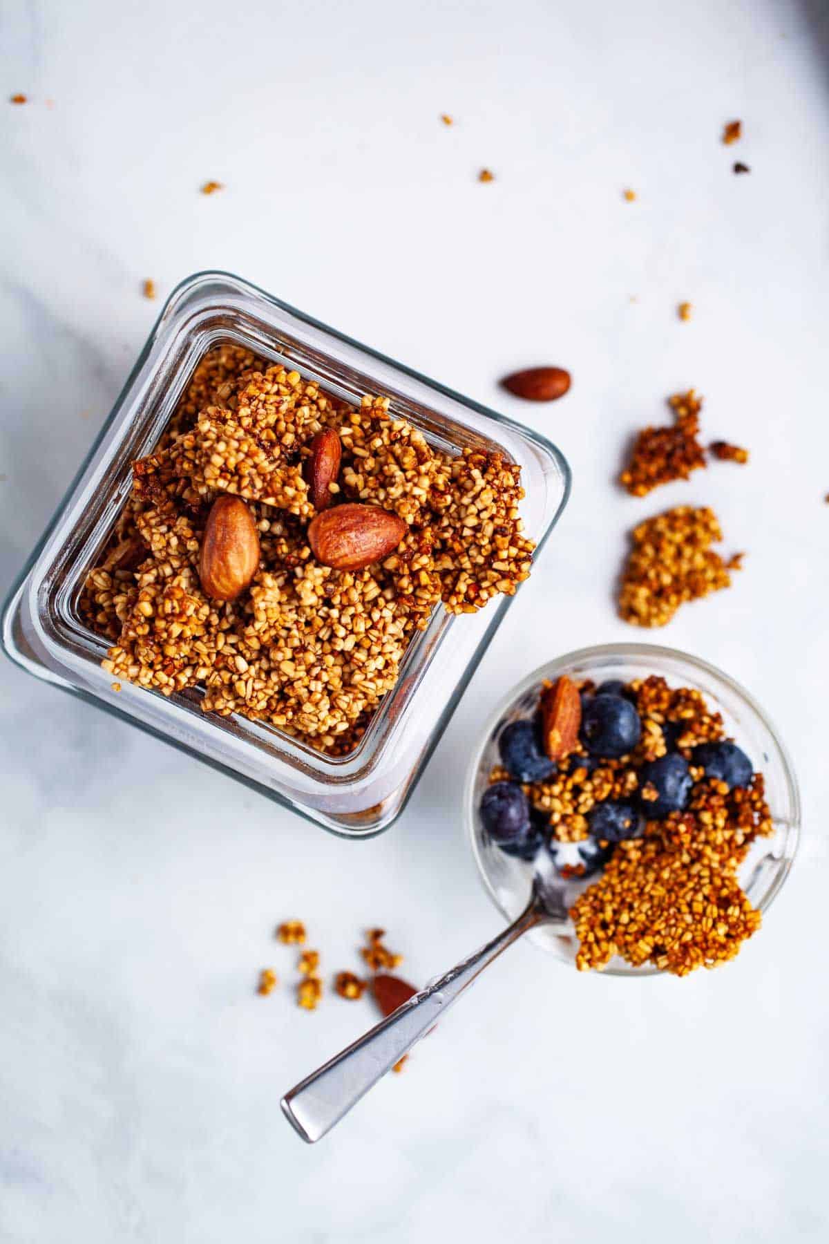 Overhead view of steel cut oats granola with almonds and blueberries in glass containers on a marble surface.