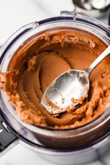 Chocolate protein ice cream freshly processed in a Ninja Creami pint container with a spoon on a marble surface.