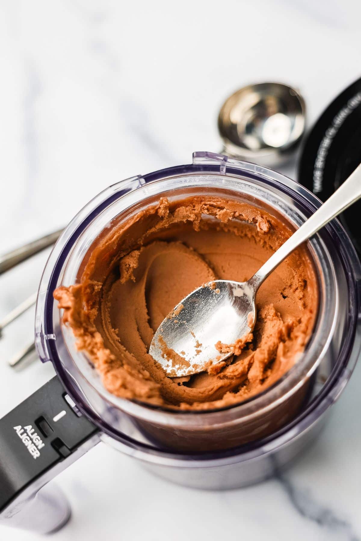 Image 1 &mdash; Hero
Chocolate protein ice cream freshly processed in a Ninja Creami pint container with a spoon on a marble surface.