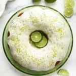 Overhead view of glazed key lime pound cake on a green plate with lime slices and lime zest on top.