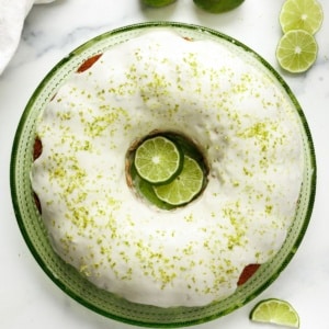 Overhead view of glazed key lime pound cake on a green plate with lime slices and lime zest on top.