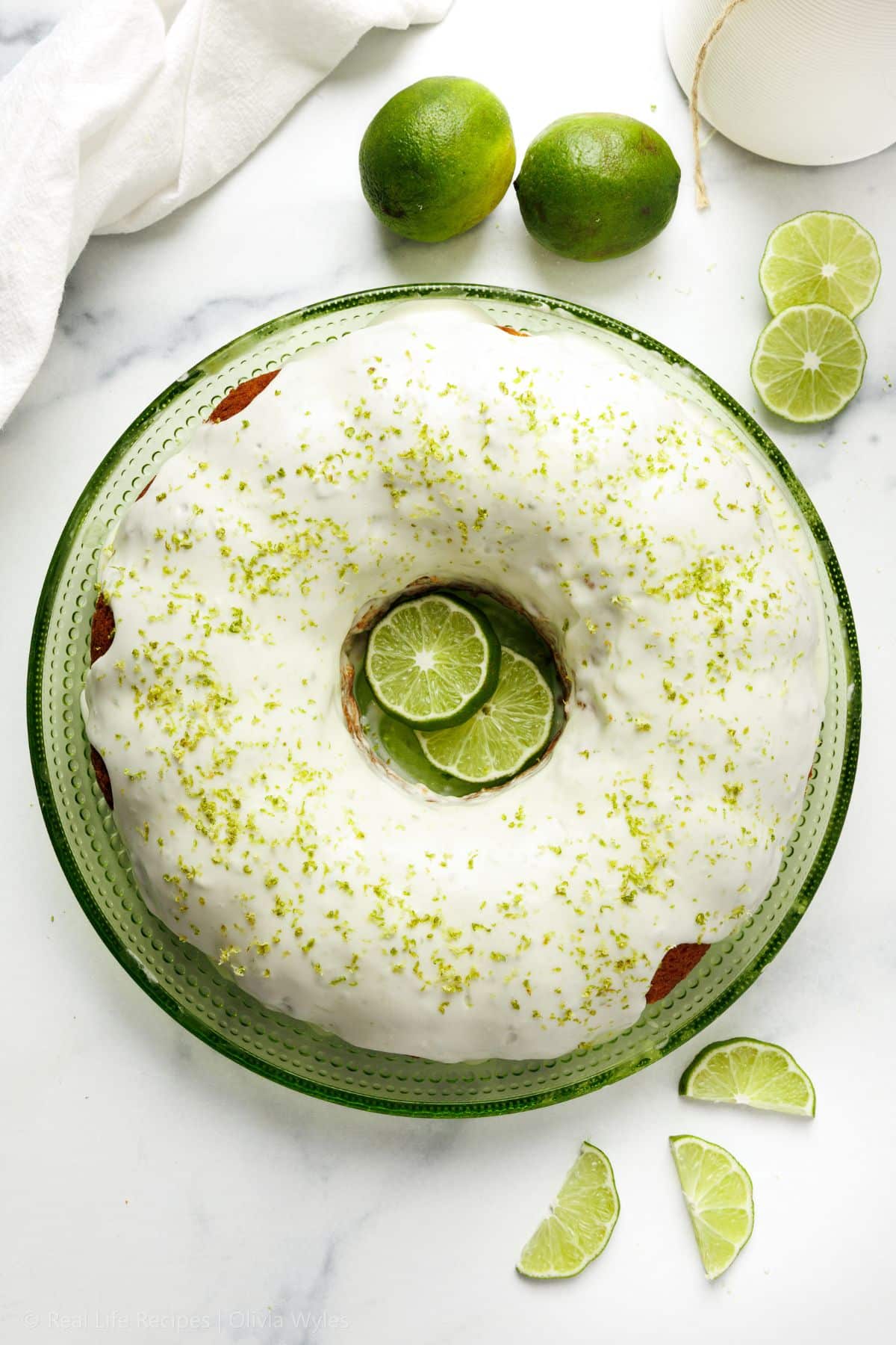 Overhead view of glazed key lime pound cake on a green plate with lime slices and lime zest on top.
