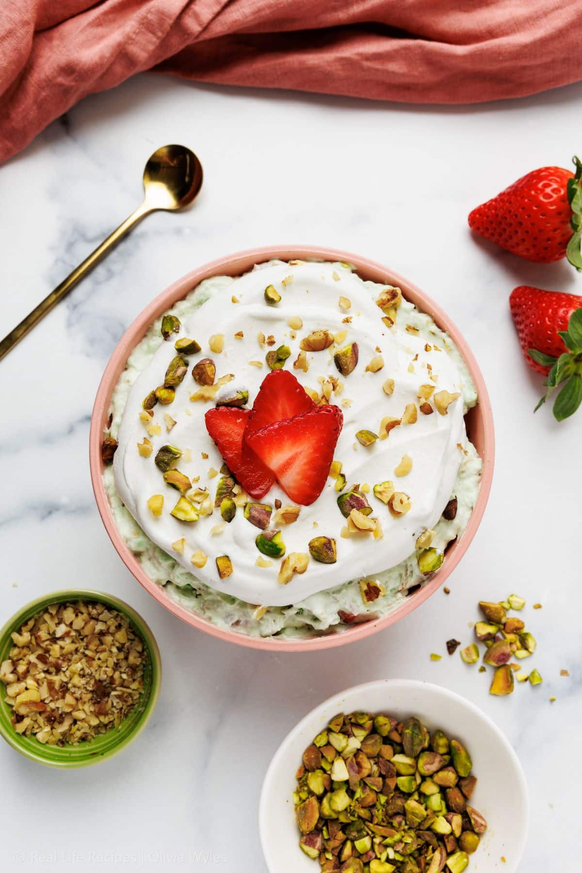 Pistachio fluff in a glass bowl, topped with strawberries and chopped pistachios.