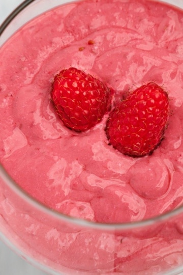 Overhead view of a raspberry pink lemonade smoothie with two fresh raspberries in a clear glass.