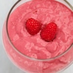 Raspberry pink lemonade smoothie in a tall clear glass topped with two fresh raspberries on a marble surface.