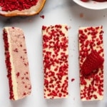no-bake white chocolate raspberry protein bars topped with freeze-dried raspberry pieces on a marble surface.