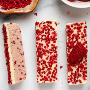 no-bake white chocolate raspberry protein bars topped with freeze-dried raspberry pieces on a marble surface.