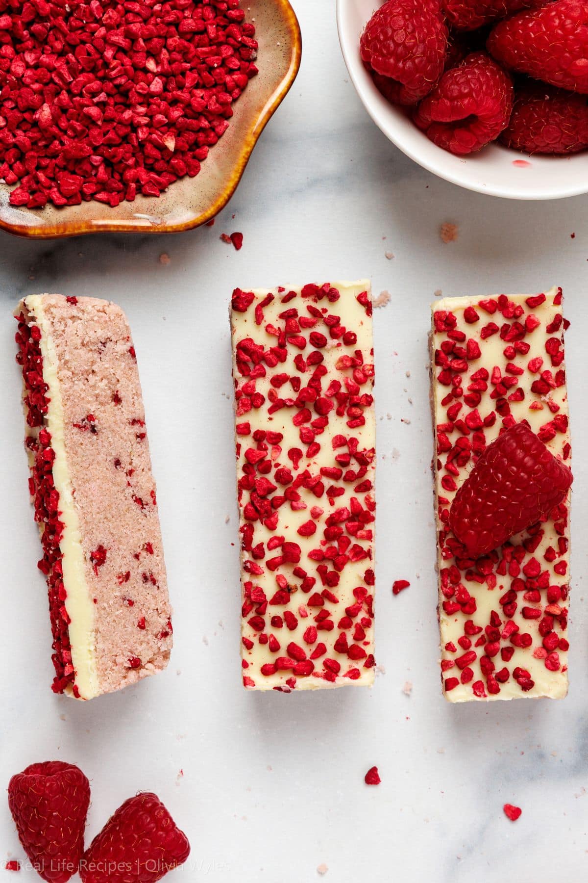 no-bake white chocolate raspberry protein bars topped with freeze-dried raspberry pieces on a marble surface.