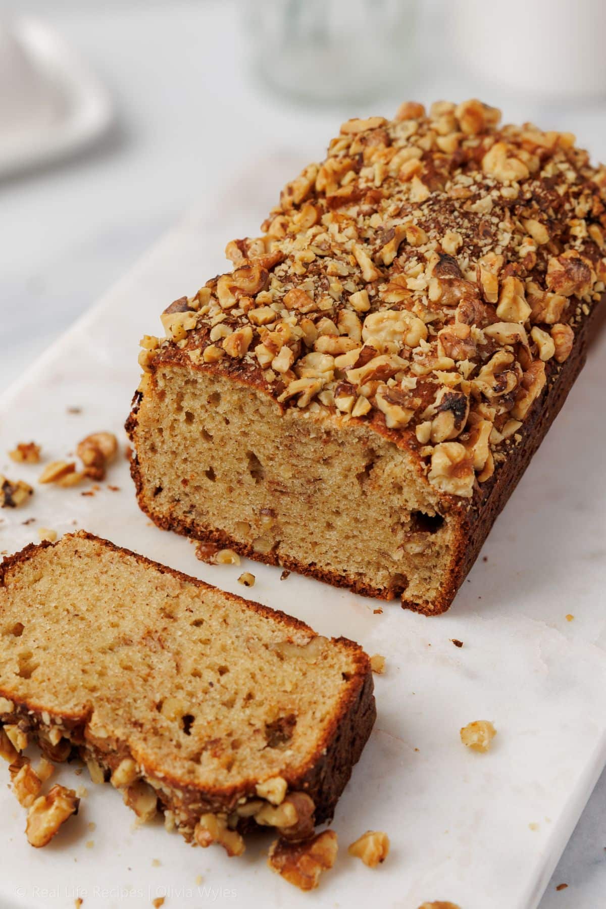 Sliced protein banana bread loaf on a marble board, with a blurred glass milk bottle in the background.